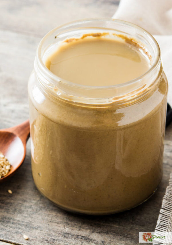 Tahini dressing in a glass jar with a spoon of sesame seeds next to it