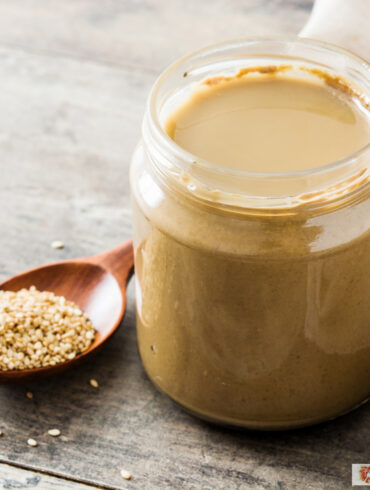 Tahini dressing in a glass jar with a spoon of sesame seeds next to it