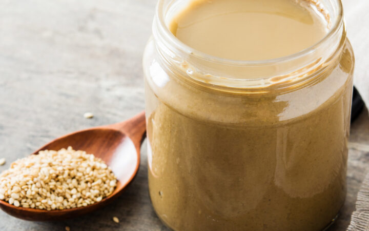 Tahini dressing in a glass jar with a spoon of sesame seeds next to it