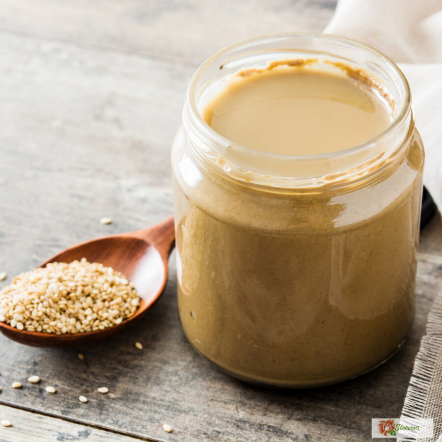 Tahini dressing in a glass jar with a spoon of sesame seeds next to it